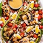 Grilled Chicken Cobb Salad on a white oval serving platter. A small gray bowl of honey dijon dressing in on the platter.