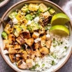 Honey Chipotle Chicken Rice Bowl topped with lime wedges, avocado corn salsa and crumbled queso fresco.