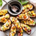 Peach Corn Ricotta Crostini on a gray plate with balsamic glaze in a bowl.