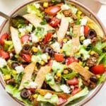 Taco salad bowl with avocado dressing drizzled on top and tortilla strips.