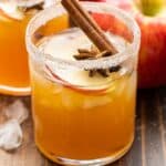 Apple Cider Margarita with a cinnamon stick, apple slices, and star anise in the glass. Two red apples behind it.