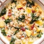 Overhead photo of sausage potato and kale soup in a white bowl with a spoon.