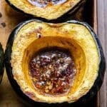 A halved Maple Roasted Acorn Squash filled with melted butter, maple syrup, and pecans.