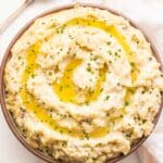 Mashed potatoes topped with melted butter and chives in a white serving bowl.