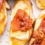 Closeup photo of baked brie crostini topped with crispy prosciutto and honey.