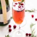 Cranberry Champagne Cocktails with a bottle of champagne next to them and rosemary and cranberries on the counter.