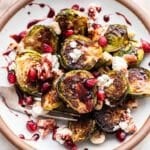 Pomegranate Brussels Sprouts on a white plate with a fork.