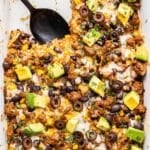 Ground Beef Taco Casserole in white dish with a piece cut out and a black serving spoon in it's spot.