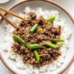 White bowl full of rice and Mongolian ground beef with chopsticks in it.