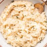Parmesan risotto in a white bowl with a spoon in it.