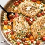 Baked chicken with feta and tomatoes in a skillet with a black serving spoon.