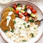 White bowl full of rice, baked falafels, tomato cucumber salad, feta, and tahini yogurt dressinfg.