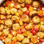 Sweet and sour chicken meatballs with pineapple, peppers, and onions in a skillet.