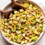 White serving bowl filled with the chicken avocado corn salad and two wooden serving spoons.