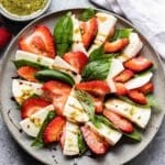 Strawberry Caprese Salad on a gray plate with a small bowl basil dressing behind it.