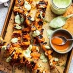 Buffalo chicken skewers on a sheet pan with a bowl of buffalo sauce and a jar of avocado ranch dressing.