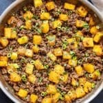 Pineapple beef stir fry in a skillet with a bowl of sesame seeds behind it.