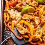 Spatula scooping up chicken fajitas off of a sheet pan.