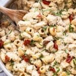 Creamy pesto chicken pasta in a skillet with a wooden spoon.