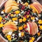 Kale salad with butternut squash, apples, feta, pomegranate seeds, and pepitas in a white serving bowl.