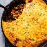 Tamale pie with a portion scooped out and a black serving spoon in the skillet.
