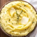 Mashed potatoes with melted butter on top and fresh thyme leaves.