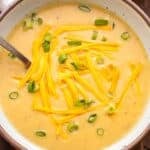 Potato soup in a white bowl topped with shredded cheddar cheese and sliced scallions.
