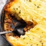 Shepherds pie in a cast iron skillet with a portion cut out and a black serving spoon in it's place.