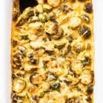 Brussels sprouts gratin in a white casserole dish with a black spoon.