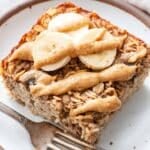 A slice of Banana Bread Baked Oatmeal topped with peanut butter on a white plate with a fork.