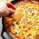 Hand dipping a tortilla chip into a skillet of beef enchilada dip.