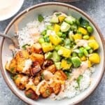 Sweet chili salmon on top of rice with mango cucumber salsa in a white bowl with a fork.