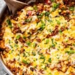 Wooden spoon in a stainless steel skillet with Mexican Chicken and Rice topped with melted cheese.