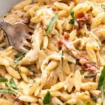 Creamy pesto orzo with sun dried tomatoes and chicken in a bowl with a fork.