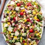 Italian Chopped Salad on an oval serving platter with wooden serving spoons next to it.