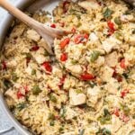 Pesto chicken and rice topped with parmesan cheese and basil in a pan with a wooden spoon.