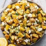 Lemon Roasted Potatoes with feta and herbs in a bowl with a halved lemon in front of the bowl.