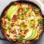 Vegetarian enchilada skillet topped with melted cheese, sliced jalapeño and avocado slices.