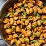 Honey garlic chicken in a skillet topped with scallions and sesame seeds.