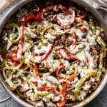 Philly cheesesteak with peppers, onions, and mushrooms in a skillet. A wooden spoon is behind the skillet.