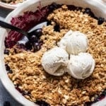 Blueberry crisp with a portion scooped out. Three scoops of vanilla ice cream on top.