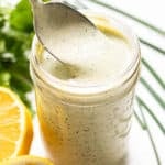 Spoon scooping ranch dressing out of a jar.