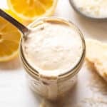 Caesar dressing in a jar with a spoon and halved lemons behind it.
