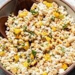 Mexican street corn pasta salad in a white serving bowl with wooden serving spoons in it.