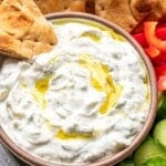 Tzatziki sauce in a bowl with a wedge of pita bread in it.