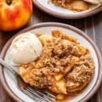 A white plate with apple crisp, vanilla ice cream, and a fork on it.