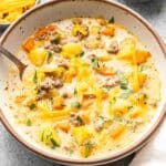 Cheeseburger soup topped with melted cheese in a white bowl with a spoon.