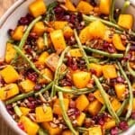 Green beans, butternut squash and pancetta salad with dried cranberries and pecans in a white serving bowl.