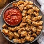 Garlic Parmesan Chicken Bites on a plate with a bowl of marinara sauce.