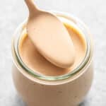 A spoon lifting balsamic dressing out of a glass jar.